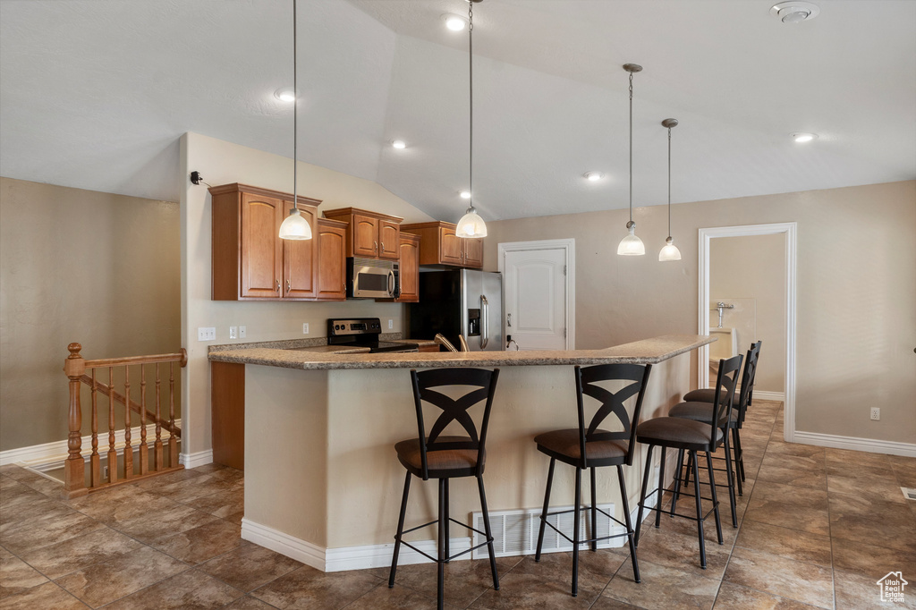 Kitchen with stainless steel appliances, lofted ceiling, a kitchen breakfast bar, pendant lighting, and brown cabinets