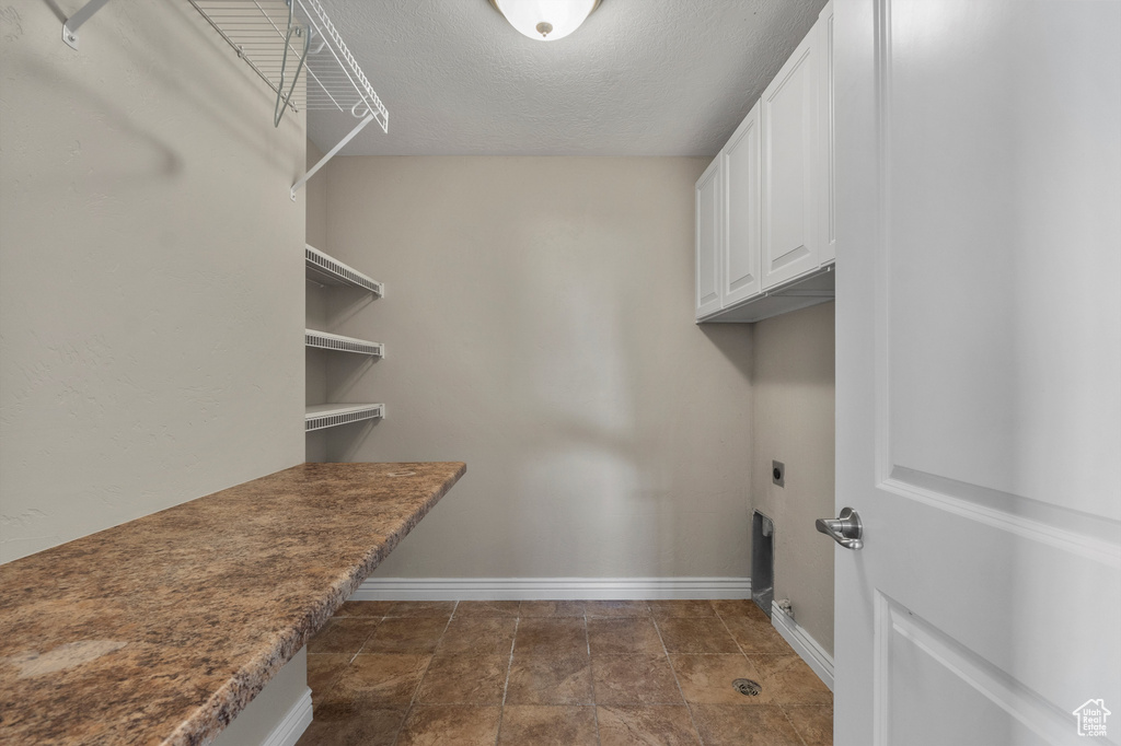 Laundry area with electric dryer hookup, baseboards, a textured ceiling, and cabinet space