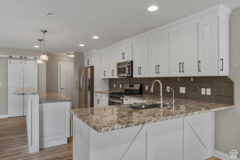 Kitchen featuring appliances with stainless steel finishes, a sink, light wood-style floors, tasteful backsplash, and baseboards