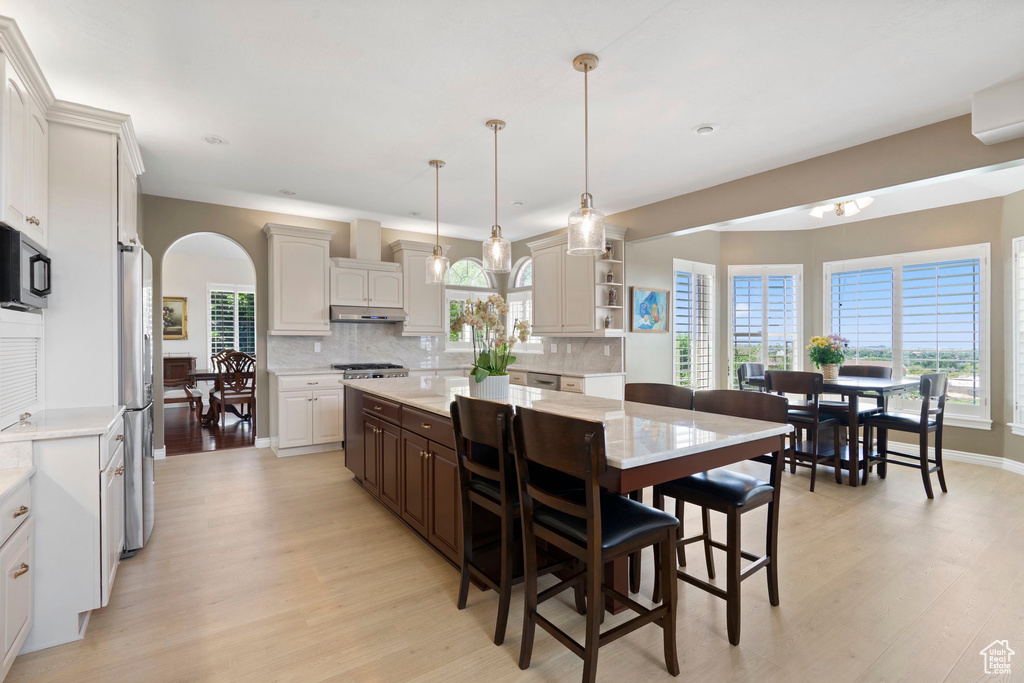 Kitchen featuring freestanding refrigerator, light wood-type flooring, under cabinet range hood, and light countertops