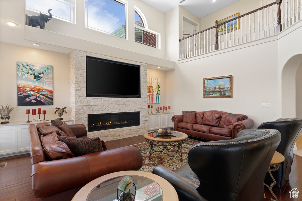 Living room with a towering ceiling, wood finished floors, a fireplace, arched walkways, and recessed lighting