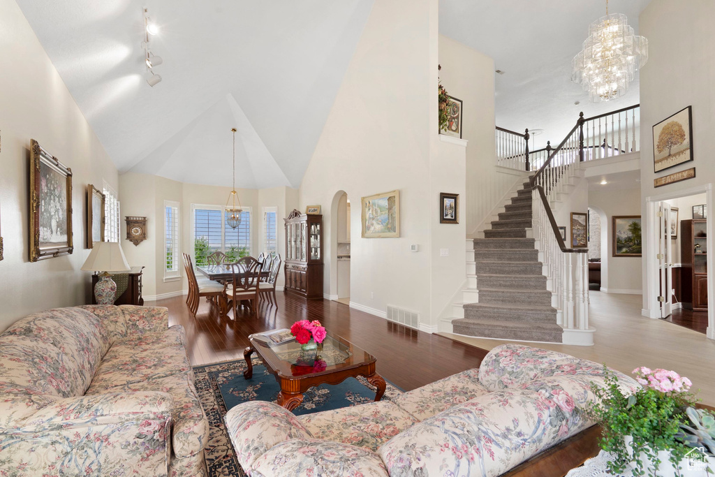 Living area with a high ceiling, a chandelier, stairs, arched walkways, and wood finished floors