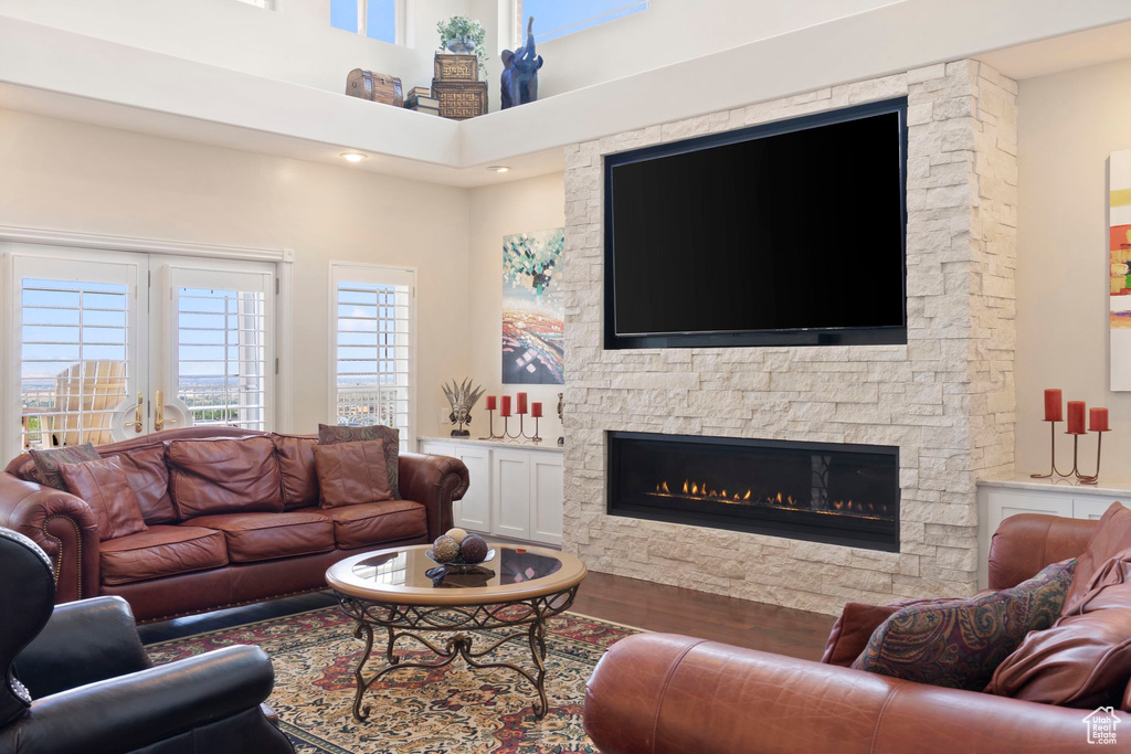 Living room featuring a stone fireplace, a high ceiling, and wood finished floors