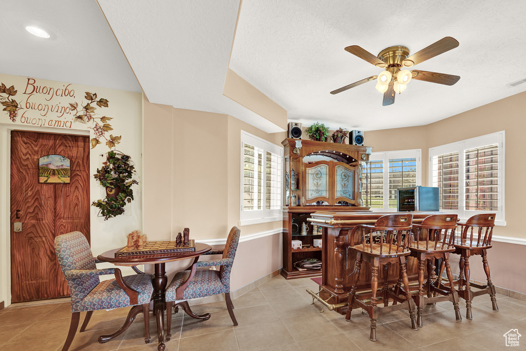 Dining area with ceiling fan, baseboards, a bar, light tile patterned floors, and a textured ceiling