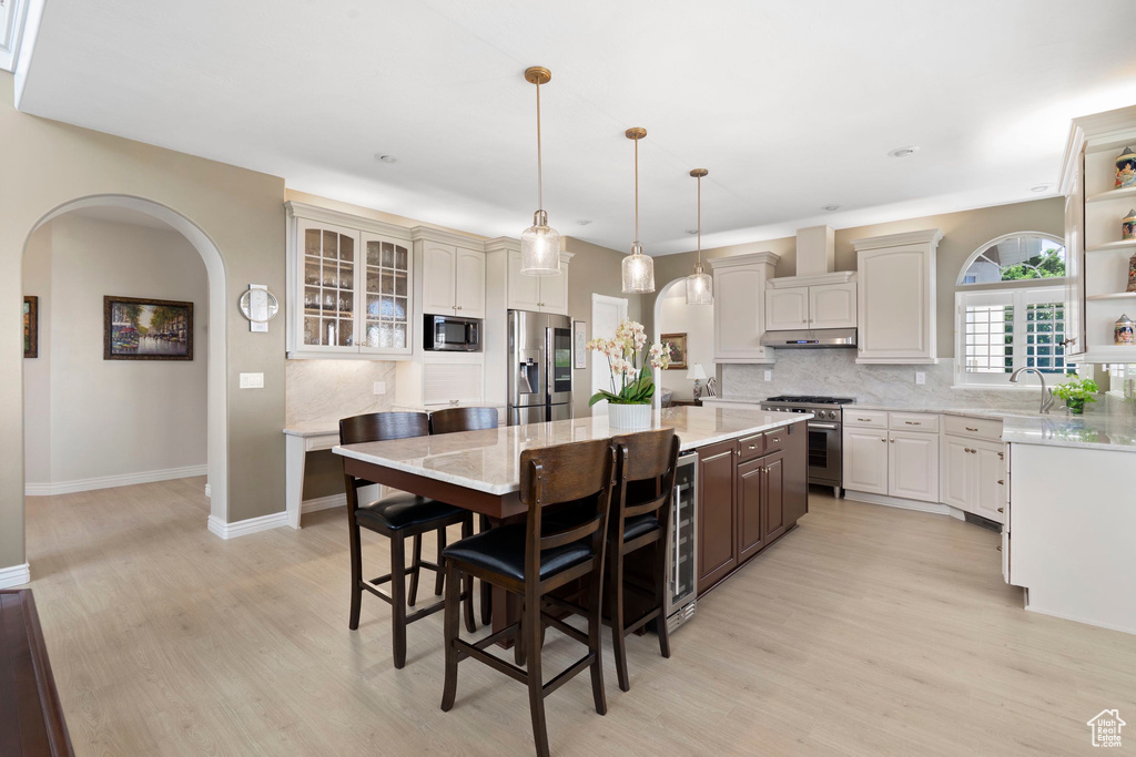 Kitchen featuring appliances with stainless steel finishes, backsplash, a center island, and light wood finished floors
