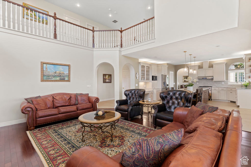 Living area with arched walkways, light wood-style floors, baseboards, recessed lighting, and a towering ceiling