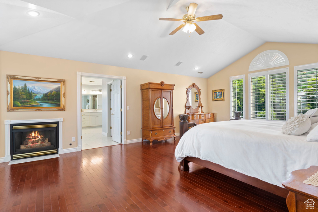 Bedroom with a glass covered fireplace, lofted ceiling, hardwood / wood-style floors, baseboards, and ensuite bathroom