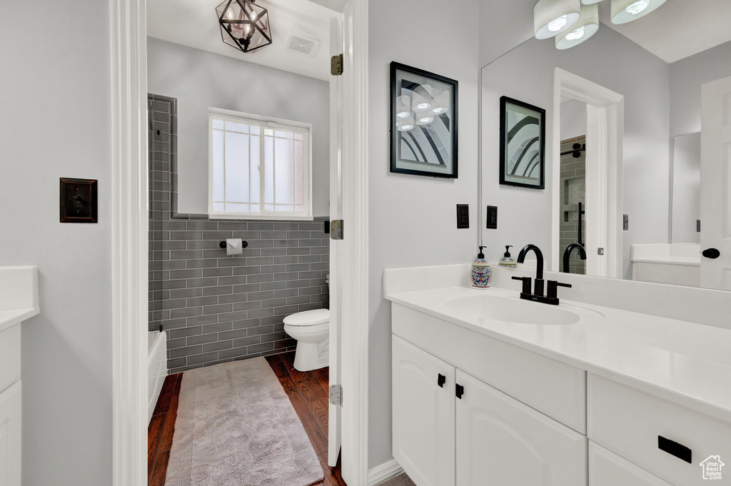 Full bathroom featuring vanity, wood finished floors, toilet, tile walls, and shower / washtub combination