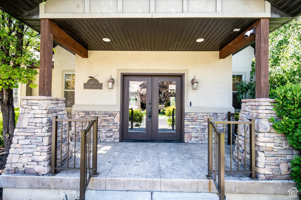 Entrance to property featuring french doors, stucco siding, stone siding, and a gate