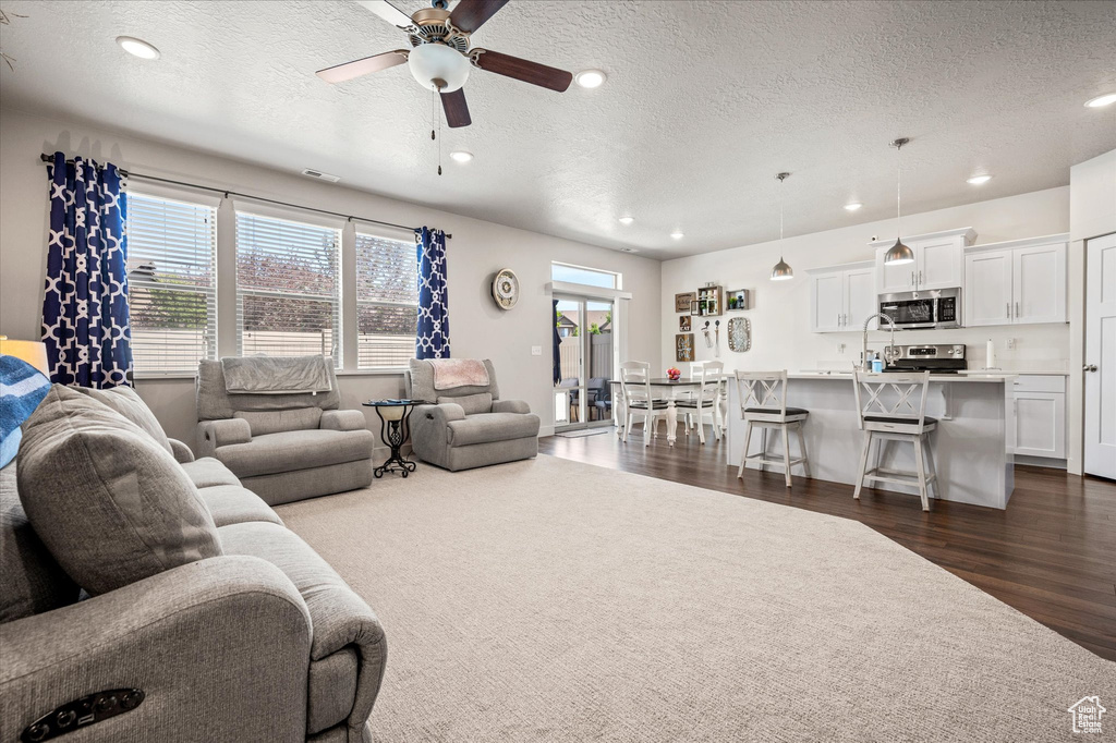 Living area with a textured ceiling, a ceiling fan, dark wood-style flooring, and recessed lighting