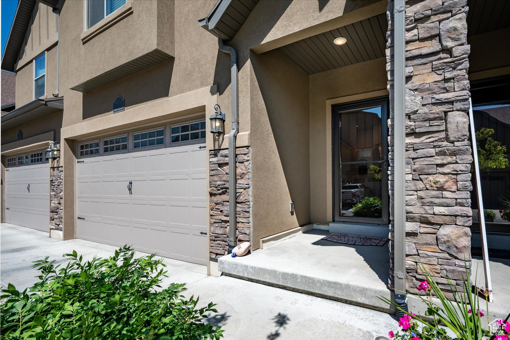 Entrance to property with stucco siding, stone siding, and an attached garage