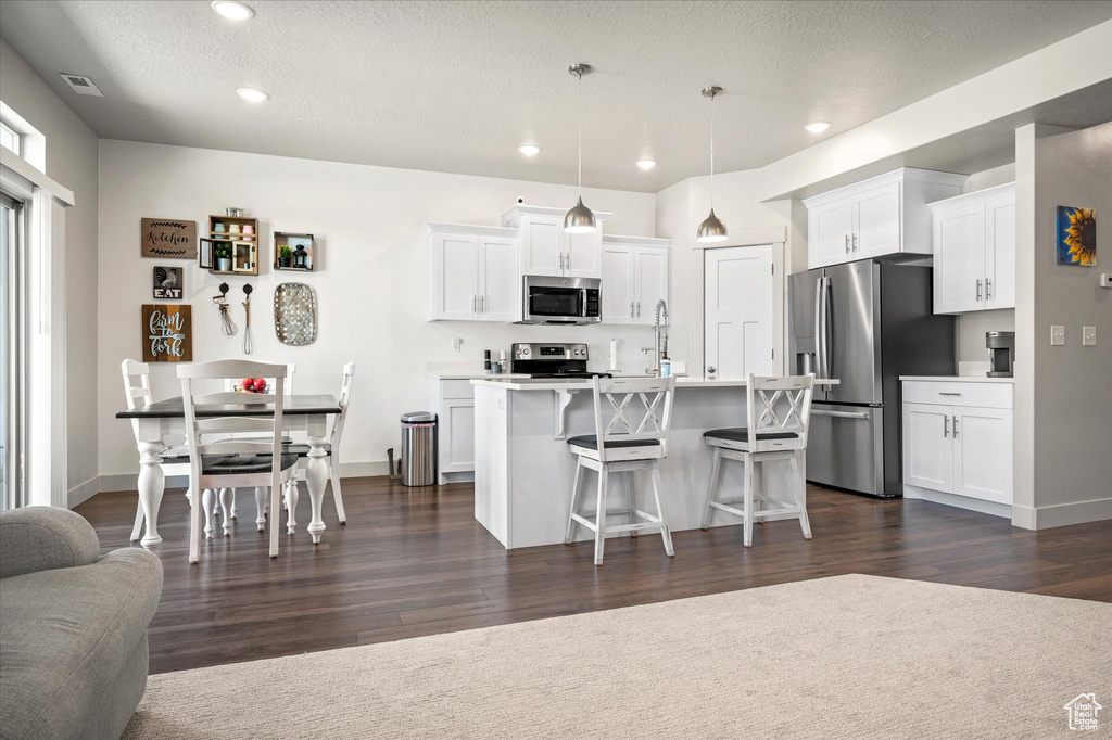 Kitchen featuring stainless steel appliances, a breakfast bar, white cabinetry, dark wood-type flooring, and recessed lighting