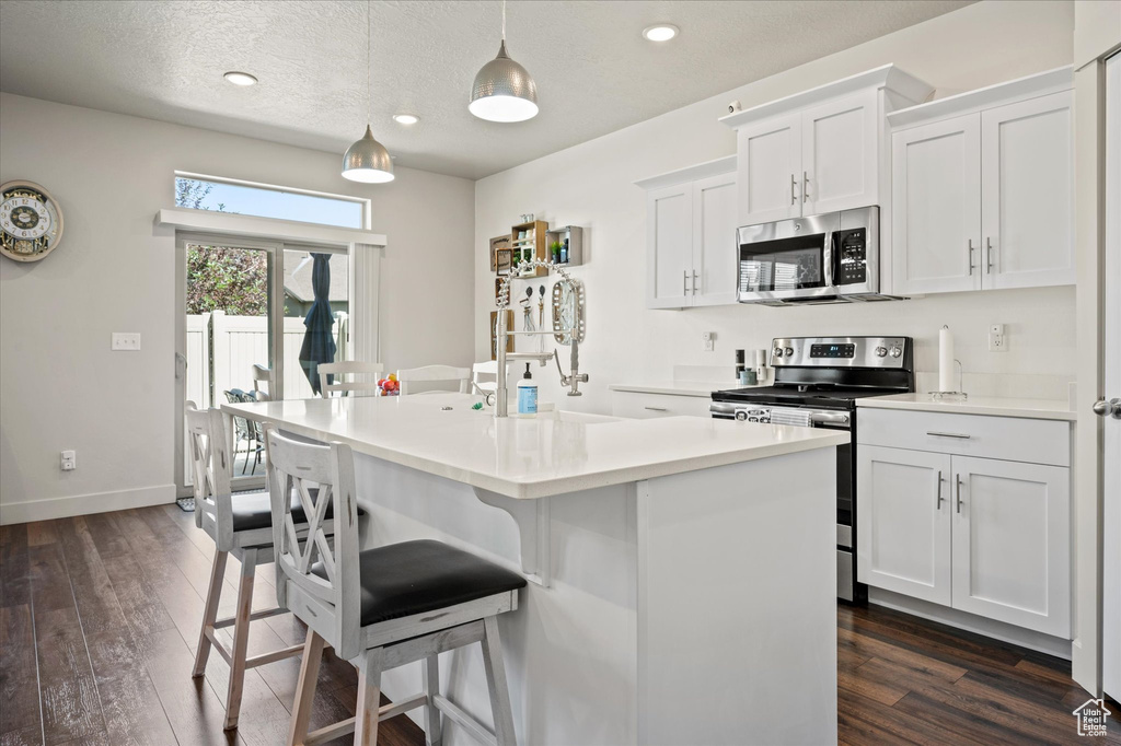 Kitchen with stainless steel appliances, dark wood-style flooring, a breakfast bar area, an island with sink, and baseboards