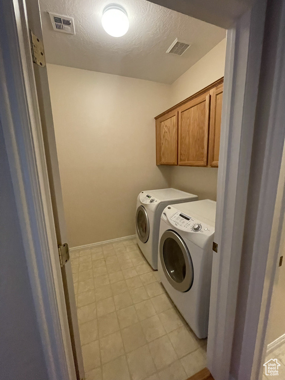 Washroom with separate washer and dryer, a textured ceiling, cabinet space, light flooring, and baseboards