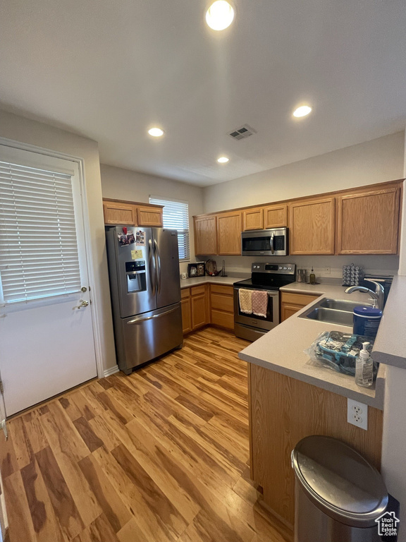 Kitchen with stainless steel appliances, a sink, light wood finished floors, light countertops, and recessed lighting