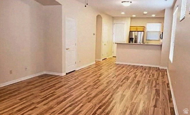 Unfurnished living room with arched walkways, wood finished floors, and baseboards