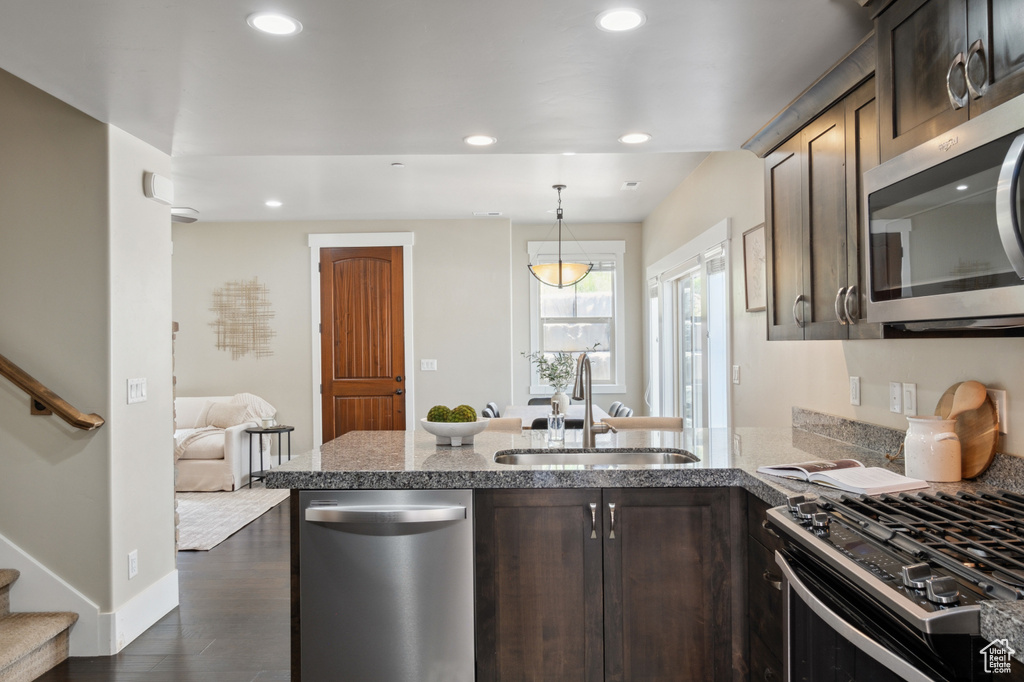 Kitchen with appliances with stainless steel finishes, a sink, dark brown cabinets, a peninsula, and light stone countertops
