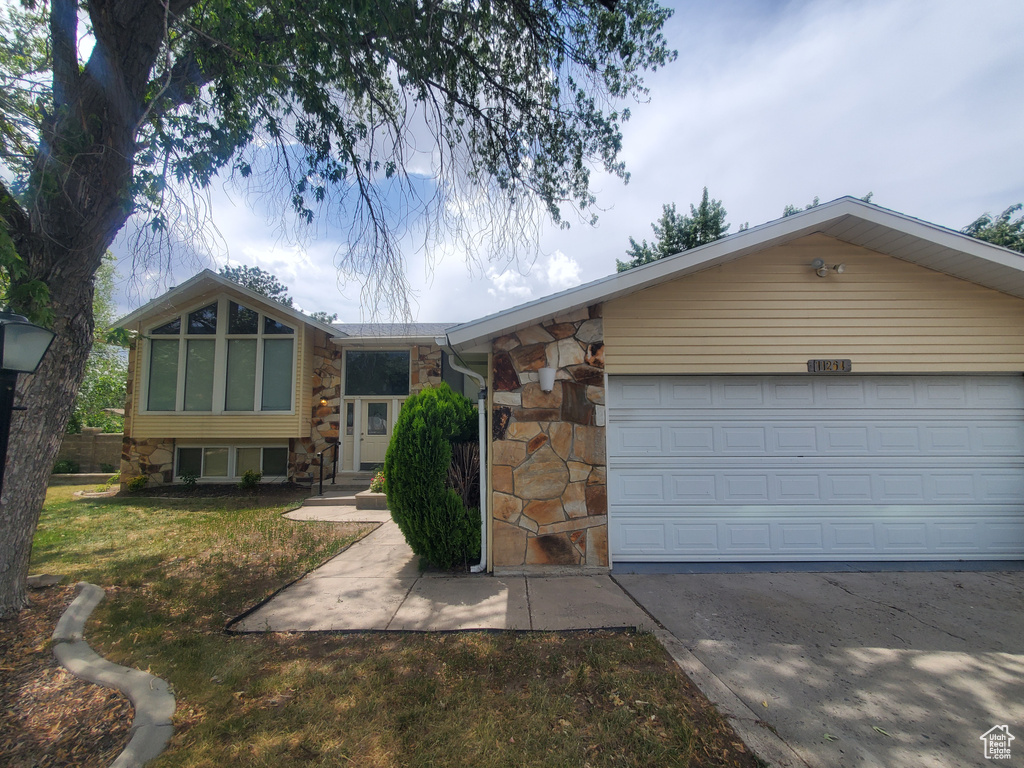 View of front of house with stone siding, an attached garage, driveway, and a front lawn