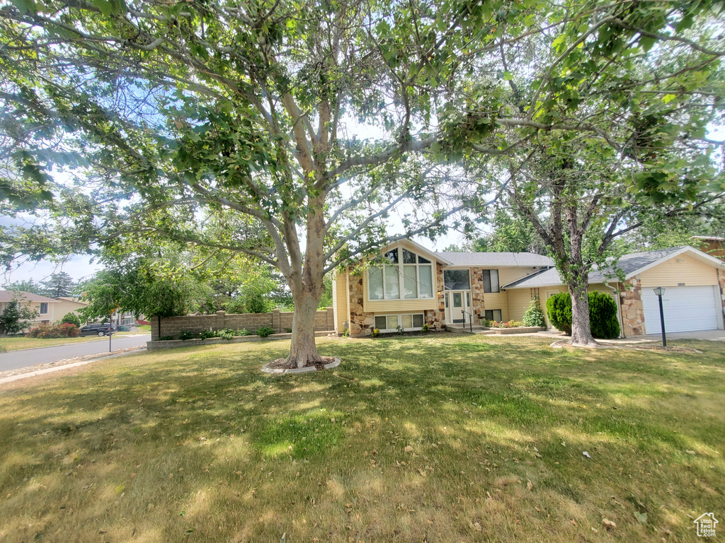 Split level home featuring a front lawn, stone siding, and an attached garage