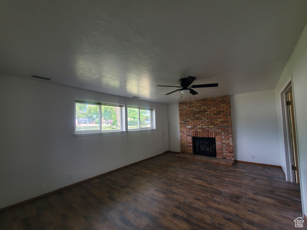 Unfurnished living room with dark wood-style floors, a ceiling fan, baseboards, and a fireplace