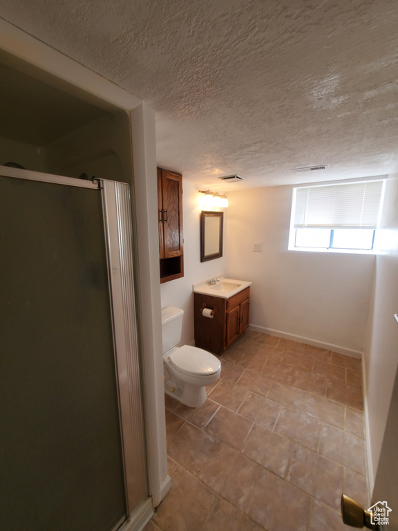 Bathroom featuring vanity, a shower stall, toilet, a textured ceiling, and baseboards