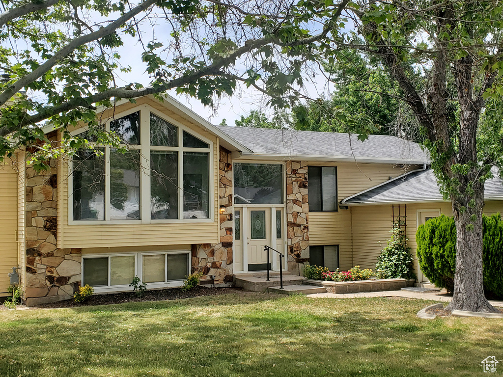 Split foyer home with stone siding, a shingled roof, and a front lawn