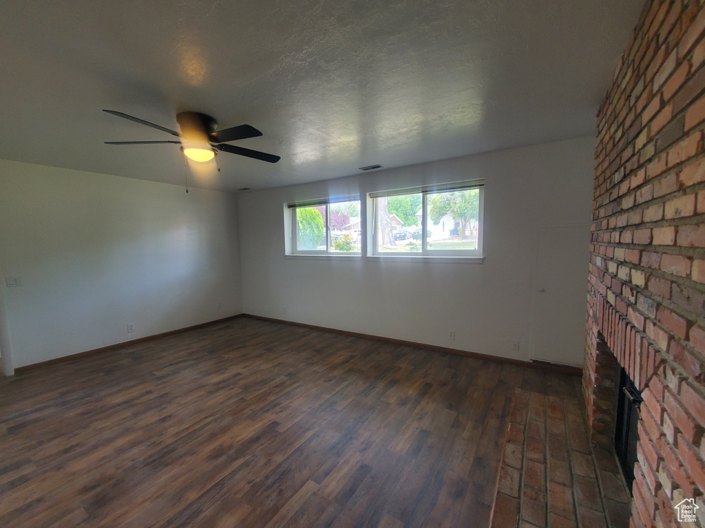 Unfurnished room with ceiling fan, a fireplace, dark wood-style floors, and baseboards