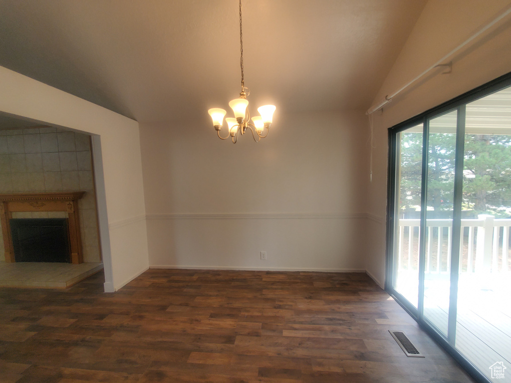 Unfurnished dining area with lofted ceiling, wood finished floors, a chandelier, and a tile fireplace