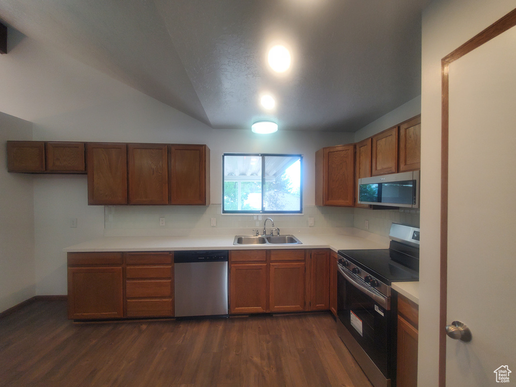 Kitchen with appliances with stainless steel finishes, a sink, dark wood-type flooring, light countertops, and backsplash
