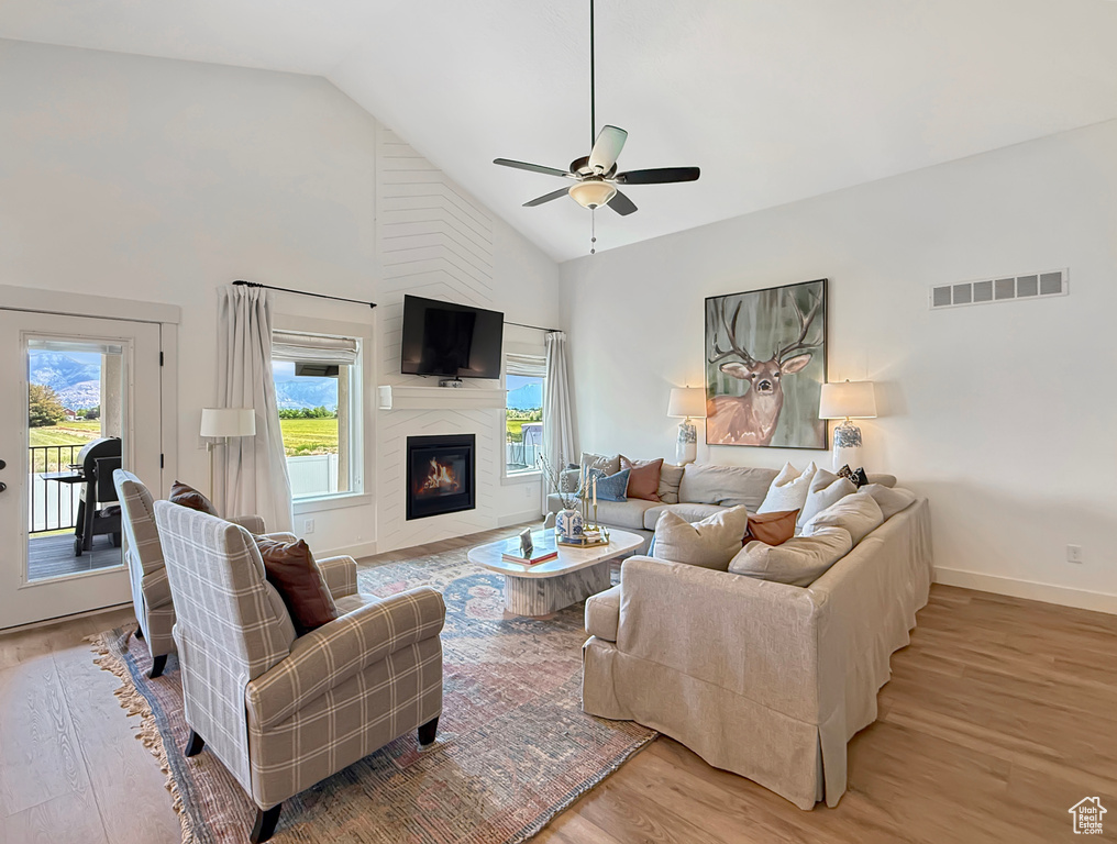 Living area with light wood-style flooring, a ceiling fan, high vaulted ceiling, a fireplace, and baseboards