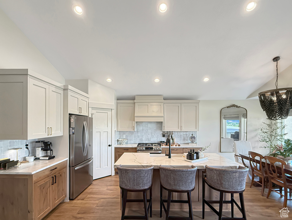Kitchen featuring appliances with stainless steel finishes, vaulted ceiling, a chandelier, a kitchen bar, and decorative backsplash
