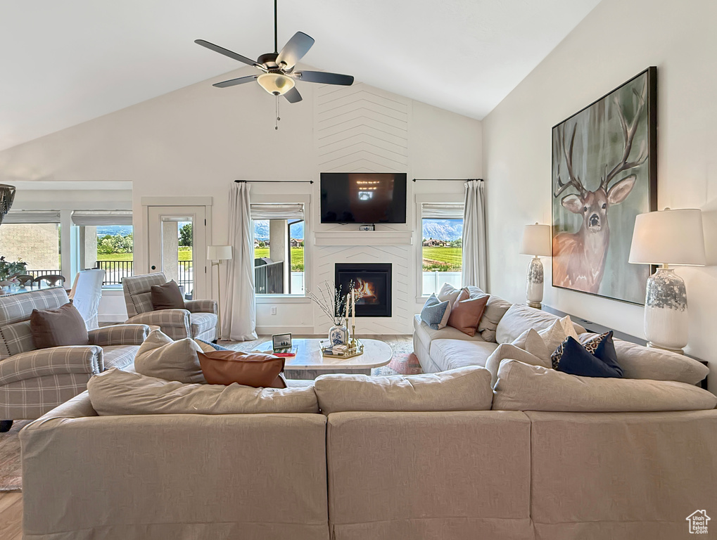 Living room with high vaulted ceiling, plenty of natural light, a premium fireplace, ceiling fan, and wood finished floors