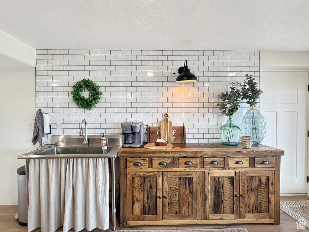 Detailed view of a sink, wood finished floors, a textured ceiling, and tasteful backsplash