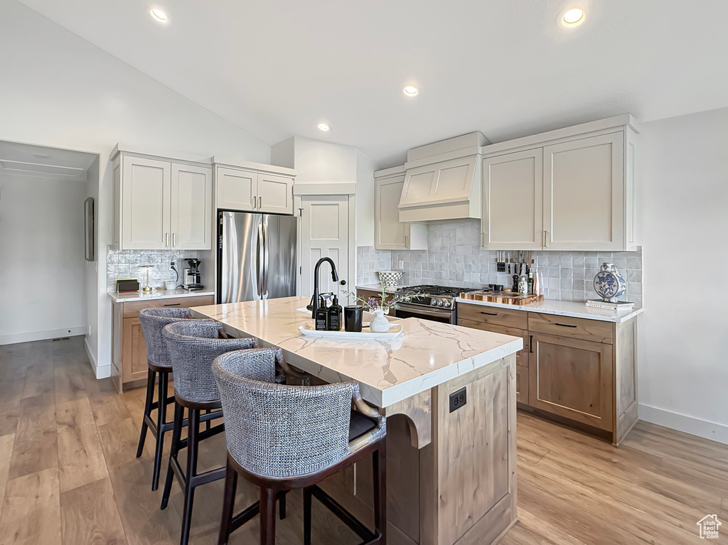 Kitchen featuring stainless steel appliances, custom exhaust hood, baseboards, light stone counters, and light wood-style floors