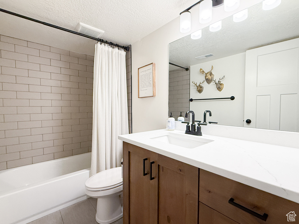 Full bathroom with a textured ceiling, vanity, toilet, shower / bath combo, and tile patterned flooring