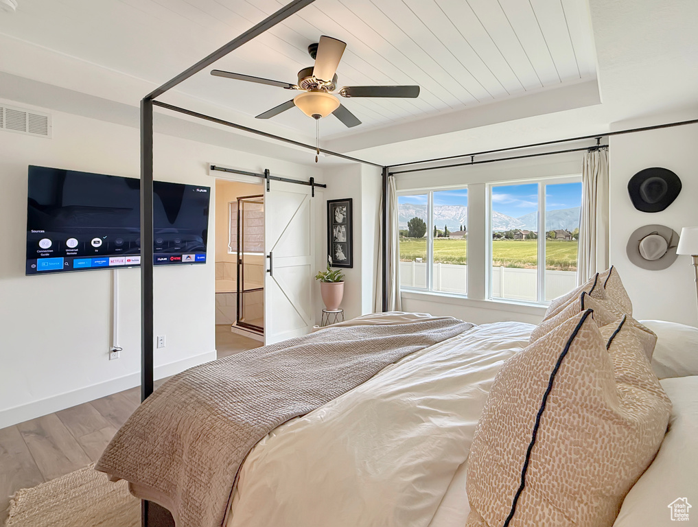 Bedroom featuring a barn door, wood finished floors, baseboards, and ceiling fan