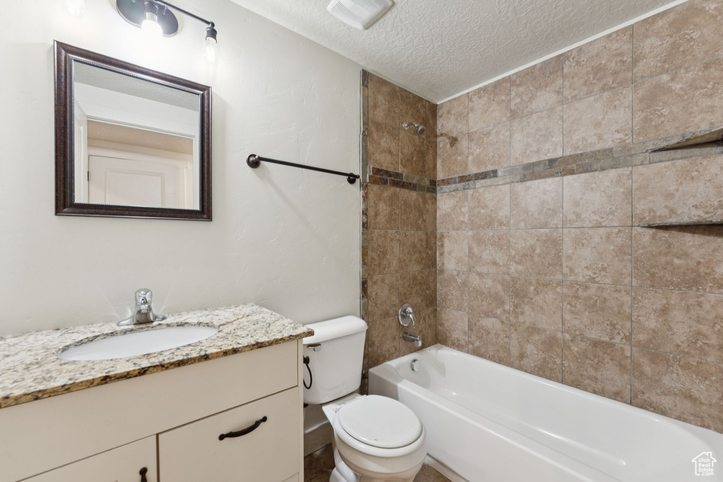 Bathroom with a textured ceiling, toilet, vanity, and washtub / shower combination