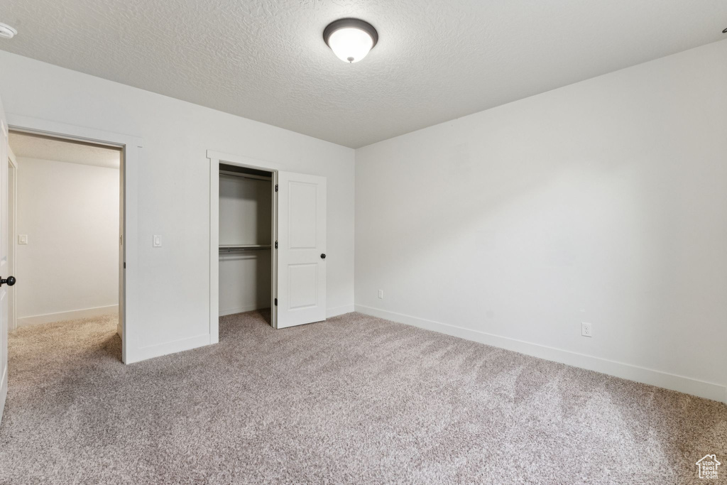 Unfurnished bedroom featuring carpet flooring, baseboards, a textured ceiling, and a closet