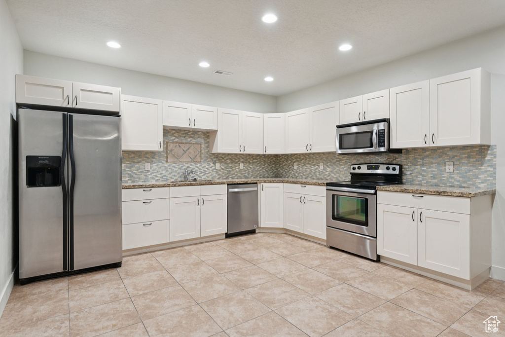 Kitchen with stainless steel appliances, a sink, backsplash, white cabinetry, and stone counters