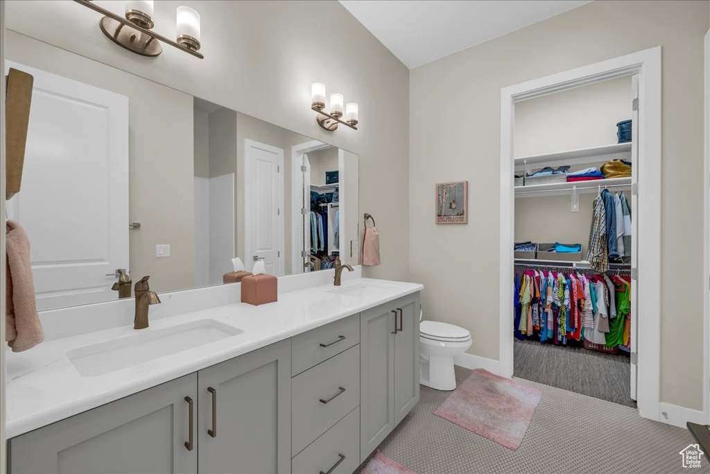 Full bathroom with double vanity, toilet, a spacious closet, and baseboards