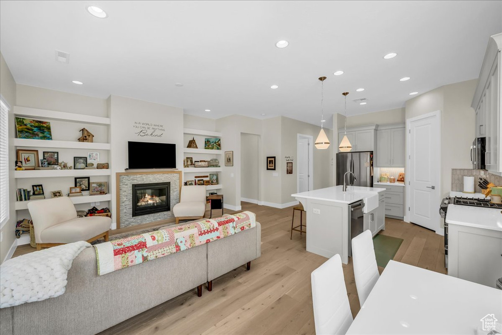 Living room featuring light wood-type flooring, a glass covered fireplace, recessed lighting, baseboards, and built in shelves