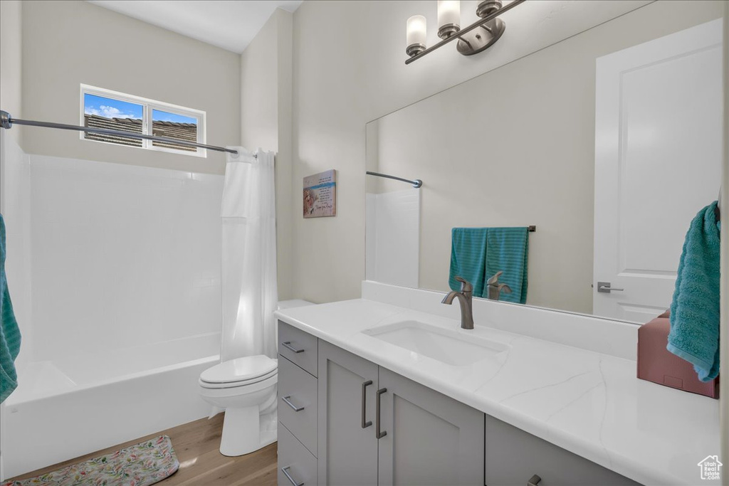Full bath with wood finished floors, vanity, shower / tub combo with curtain, and toilet