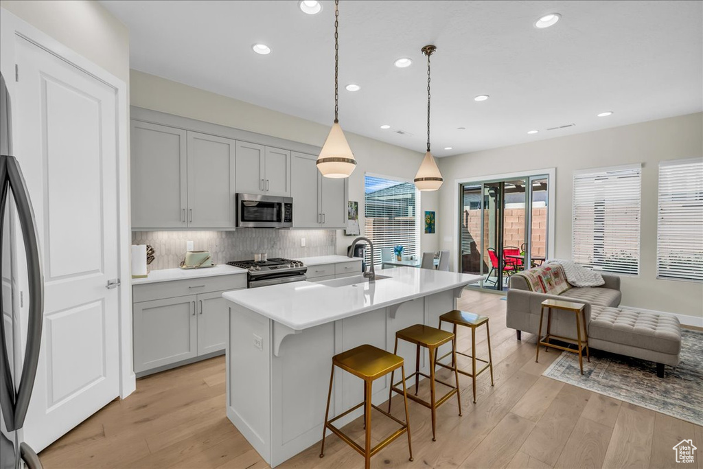 Kitchen featuring stainless steel appliances, a sink, light wood-type flooring, light countertops, and tasteful backsplash