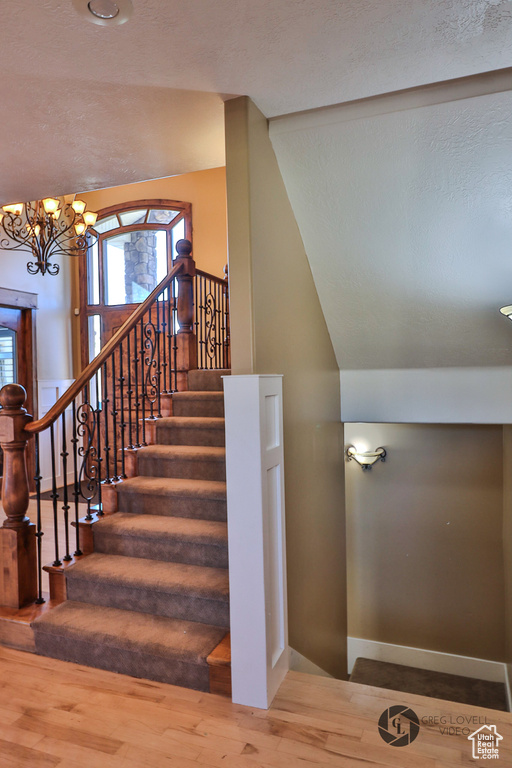 Staircase featuring a chandelier, wood finished floors, baseboards, lofted ceiling, and healthy amount of natural light