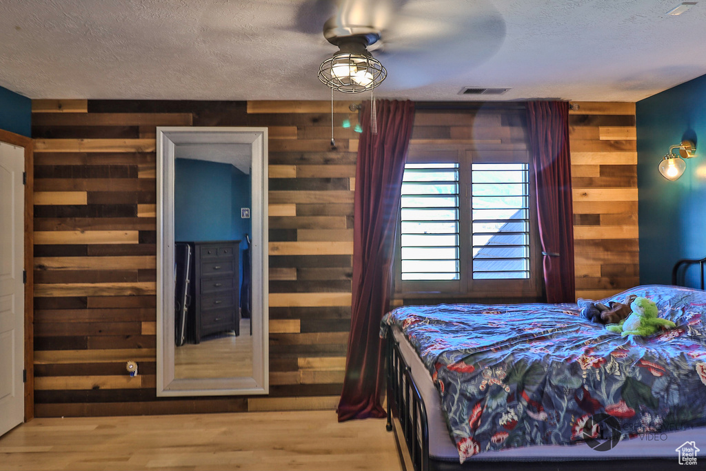 Bedroom featuring wood walls, a textured ceiling, and wood finished floors