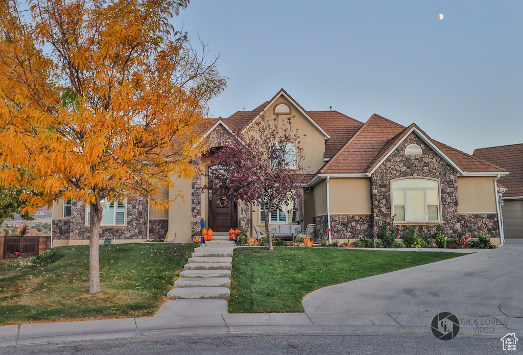 View of front of home featuring stucco siding, stone siding, a front lawn, and a tiled roof