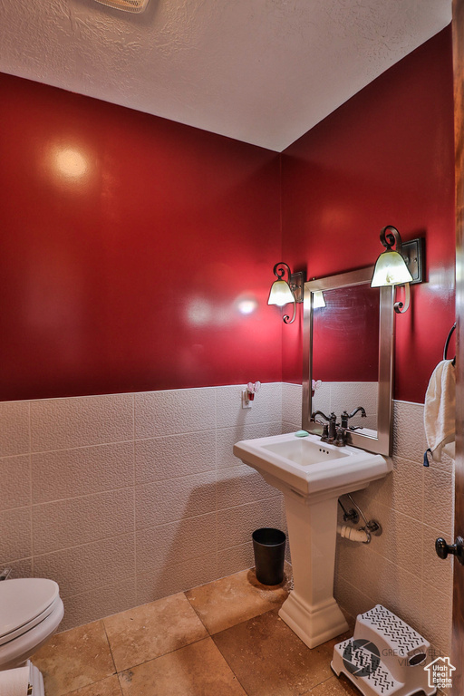 Half bathroom featuring toilet, tile walls, a sink, a textured ceiling, and a wainscoted wall