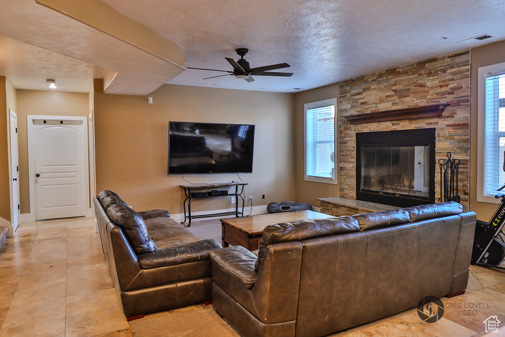 Living room featuring ceiling fan, a textured ceiling, a stone fireplace, and baseboards