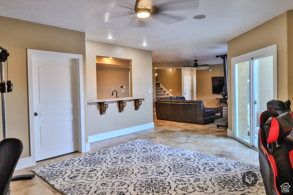 Kitchen featuring ceiling fan, open floor plan, light countertops, baseboards, and a kitchen bar
