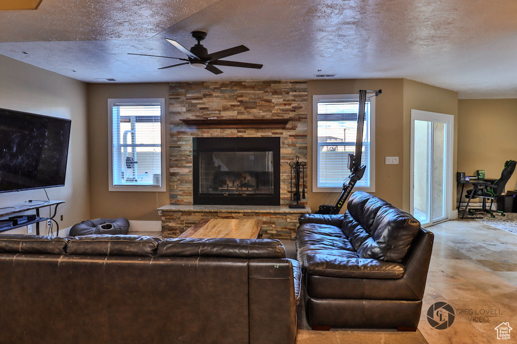Living room featuring plenty of natural light, ceiling fan, a textured ceiling, and a stone fireplace